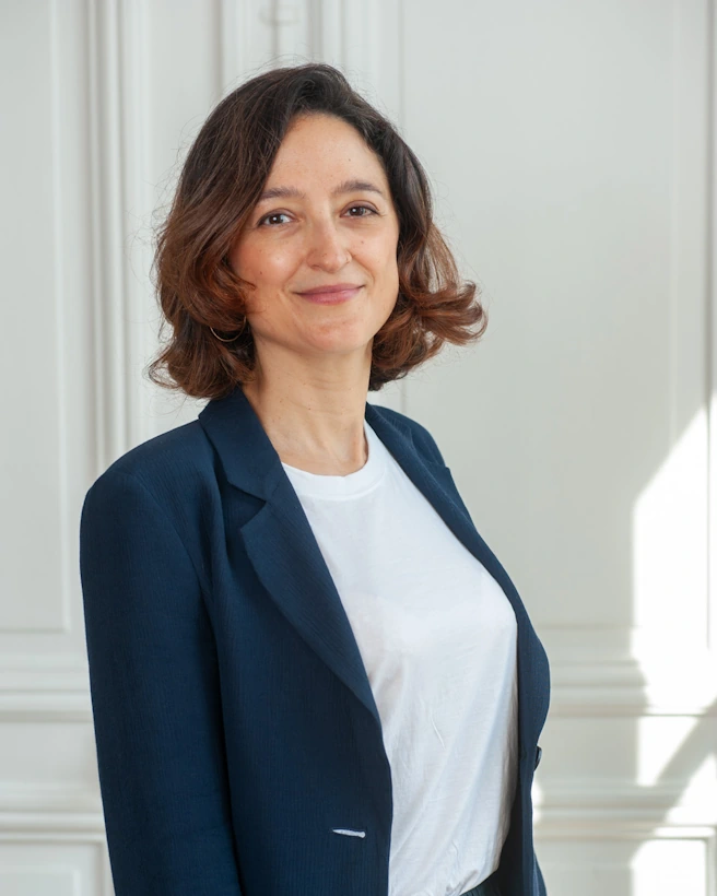 Portrait rapproché de Maître Raphaële Secnazi-Leiba souriante, dans un cadre lumineux, vêtue d’un blazer bleu et d’un t-shirt blanc