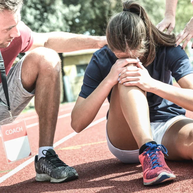 Sportive blessée au sol sur une piste avec assistance d’un coach après un accident de sport.