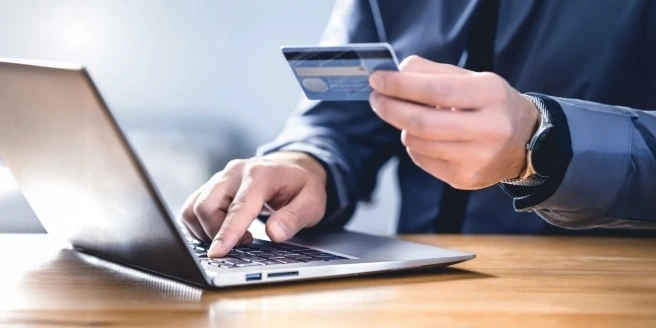 Une main tenant une carte bancaire devant un ordinateur portable.